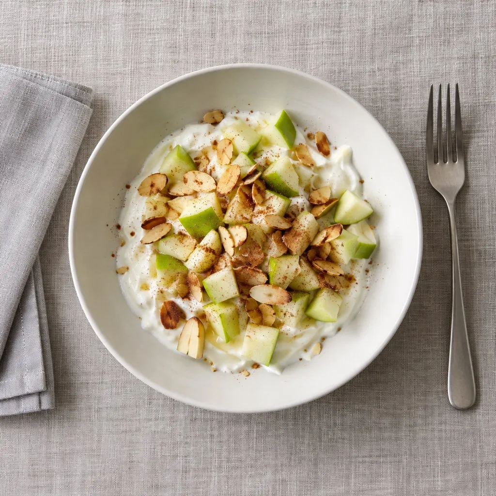 Overhead view of Greek yogurt with diced green apple, toasted sliced almonds and cinnamon in a white bowl.